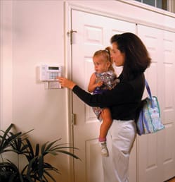 A woman holding a child and using the alarm system.